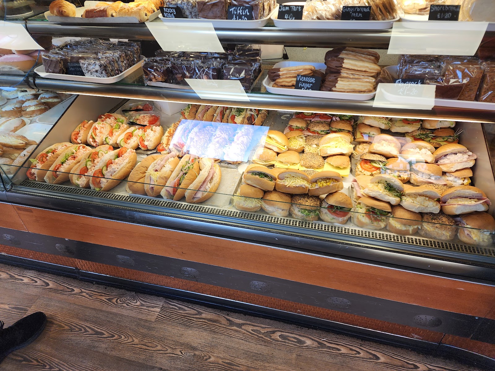 A long counter of made-to-order sandwiches and filled baps in a glass display, with patisserie behind. Photo by Zen Cheung.