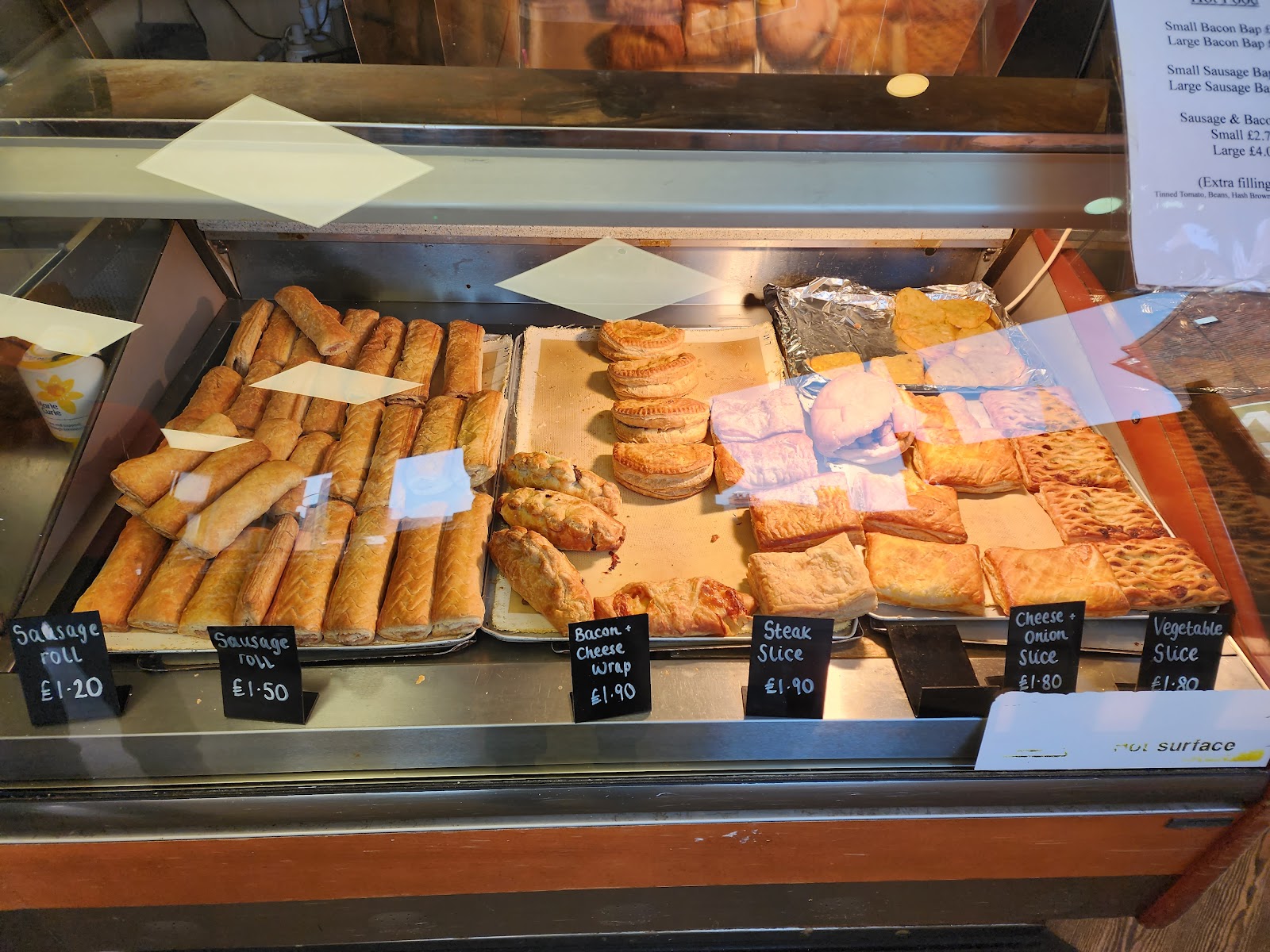 Trays of sausage rolls, bacon & cheese wraps, steak slices, cheese & onion slices and vegetable slices with chalkboard price labels. Photo by Zen Cheung.